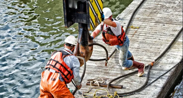 Two men pushing heavy equipment on a dock